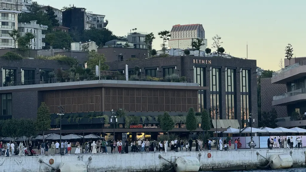 Galataport'ta bir mağaza binası; ahşap ve tuğla rengi cephe, giriş katında geniş camekânlar, önde dolaşan kalabalık ve kıyı.