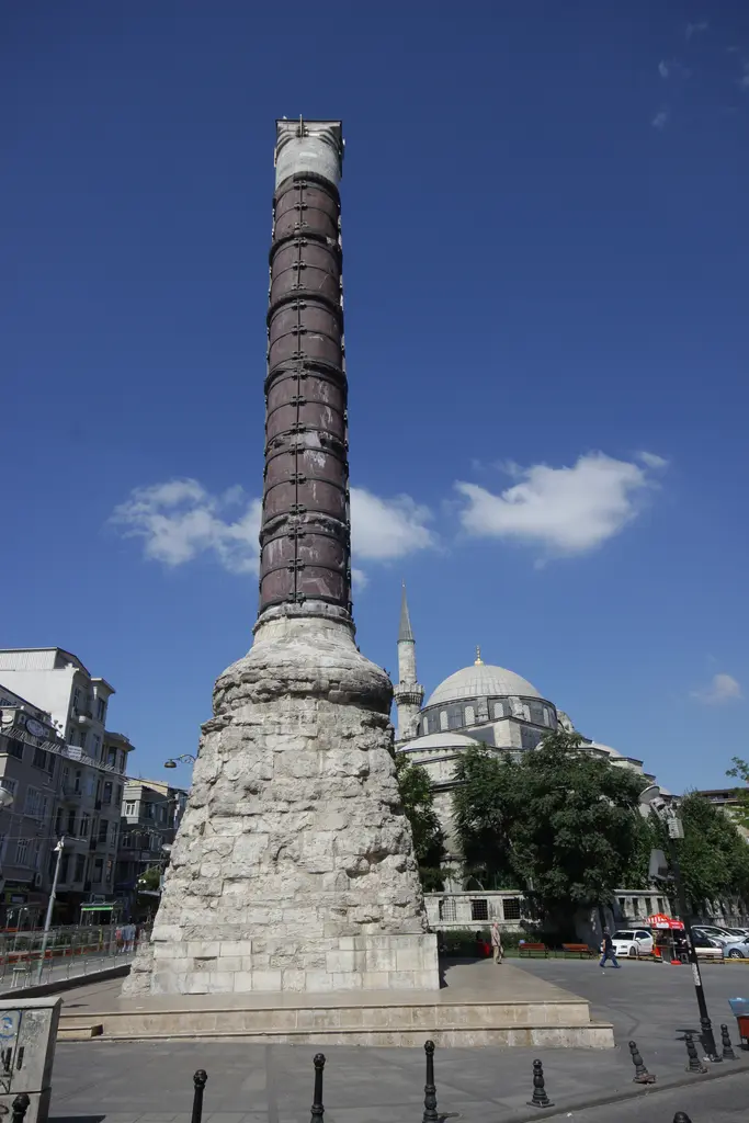 Çemberlitaş'ta sütunun tam boyu; kaideden başlığa uzanan porfir gövde, sıra sıra demir çember, arkada cami kubbesiyle minare.