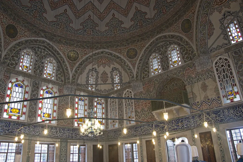 Sultan Ahmed Türbesi'nde iç mekân; kalem işli kubbe eteği, renkli camlı pencereler, avize ve kandiller, altta mavi örtülü sanduka sıraları.