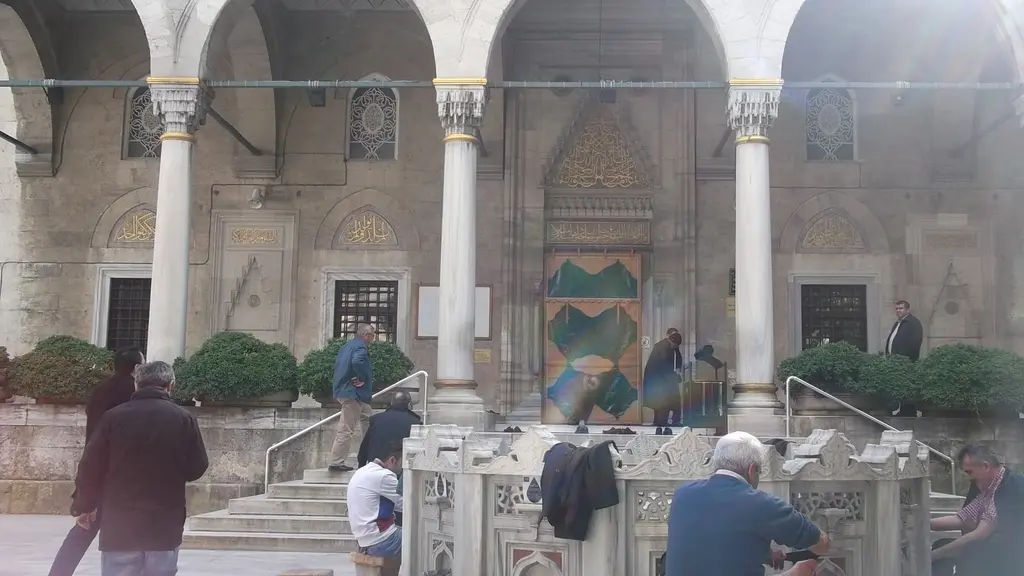 Şişli Camii'nde şadırvan başında abdest alanlar; mermer şadırvan, revak sütunları, merdiven ve arkada yeşil perdeli cümle kapısı.