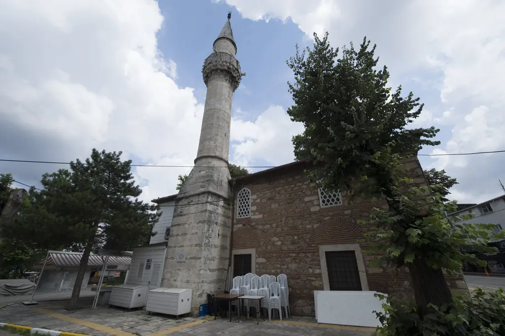 İskender Paşa Camii; taş ve tuğla örgülü gövde, kırma çatı, ince taş minare ve önünde ağaçlar.