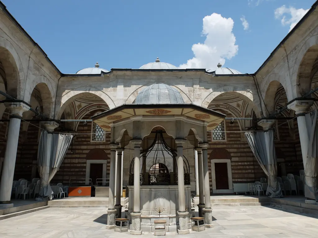 Laleli Camii'nin avlusu; ortada sütunların taşıdığı kubbeli şadırvan, çevresinde revak kemerleri ve taş döşeli zemin.