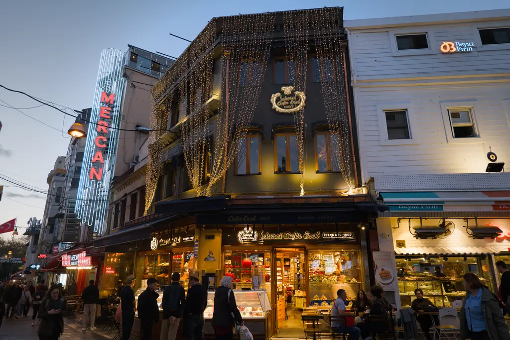 Kadıköy Çarşısı'nda Şekerci Cafer Erol; ışıklarla süslenmiş koyu renk cephe, vitrinler ve önünden geçenler.