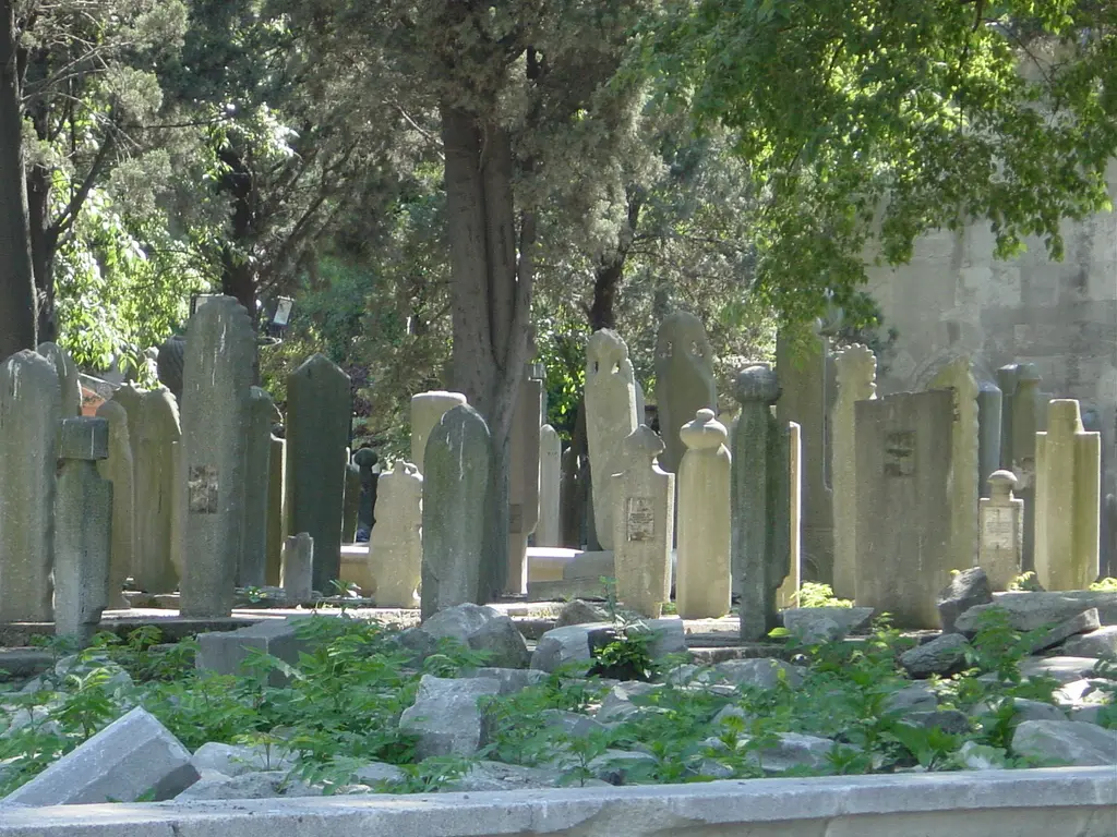 Eyüp Mezarlığı'nda kabirler; ağaçların altında sık dizilmiş eski mezar taşları, yere devrilmiş parçalar ve yeşil otlar.