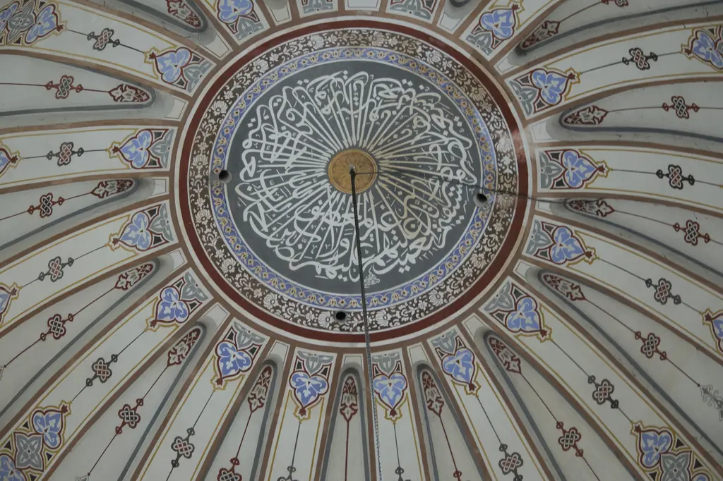 Kalenderhane Camii'nin kubbe tepesi; koyu gri zemin üzerinde ışınsal dizilmiş beyaz hat, altın göbek, rumi bordürler ve avize zinciri.