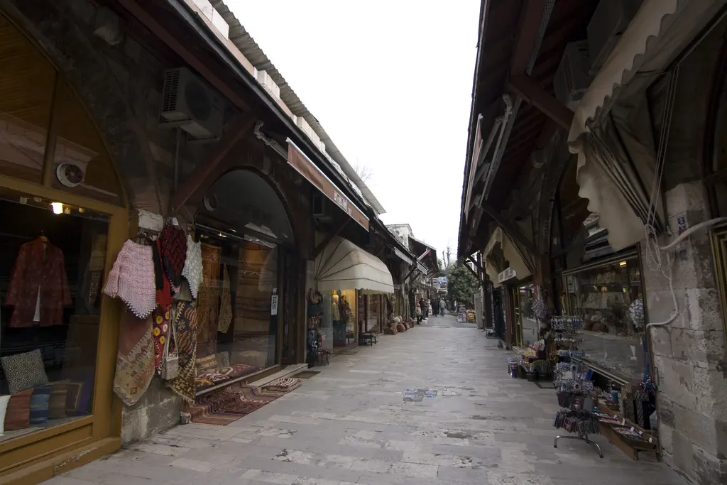 Arasta Çarşısı'nda ahşap saçaklar; kemerli dükkânların üstünde sundurmalar, vitrinlerde halılar ve sokağın iki yanına dizilen dükkânlar.