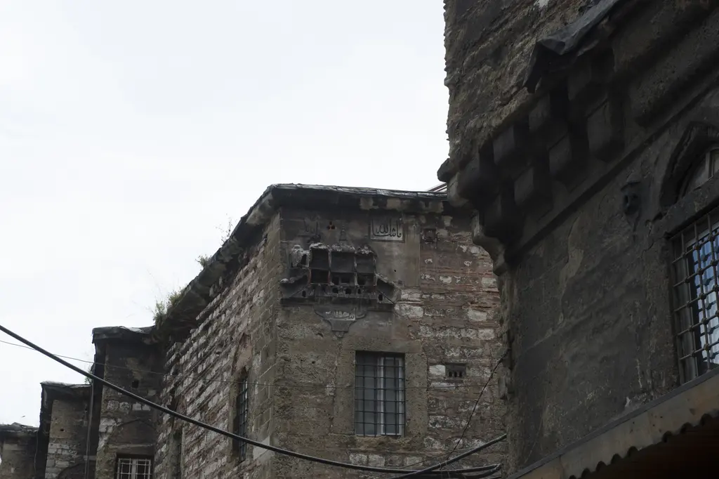 Büyük Yeni Han'ın köşesinde moloz taş duvar; demir parmaklıklı pencereler, üstte çıkma yapan kat ve önünden geçen elektrik hatları.