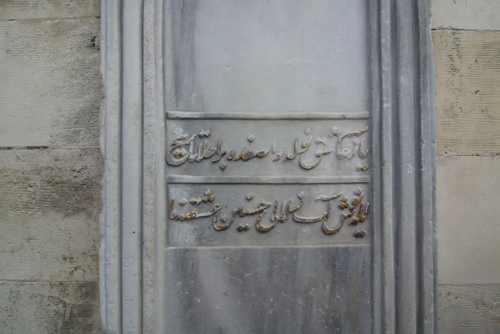 Çeşmenin mermer kitabesi yakın planda; kabartma ta'lik hatla iki satır Osmanlıca yazı ve çevresinde sade silme çerçeve.