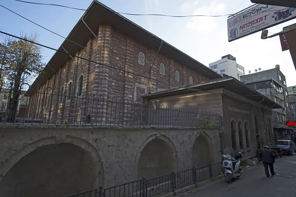 Arap Camii'nin dış cephesi; tuğla duvar, sokak seviyesinde kemerli açıklıklar, üstte pencere sıraları ve kenarda yürüyen insanlar.