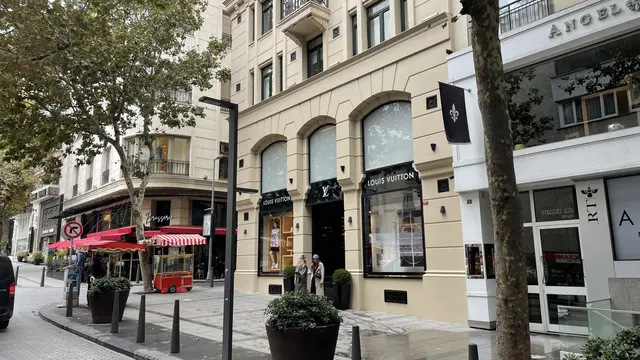 Nişantaşı'nda Abdi İpekçi Caddesi; kemerli vitrinli krem taş binalar, kırmızı beyaz tenteli bir kafe, simit arabası, çınarlar ve saksılar.