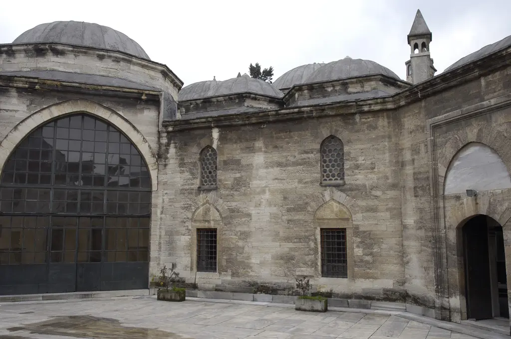 Haseki Sultan Külliyesi'nde camla kapatılmış büyük kemerli açıklık, yanında kesme taş duvar, kubbeler ve taş döşeli avlu.