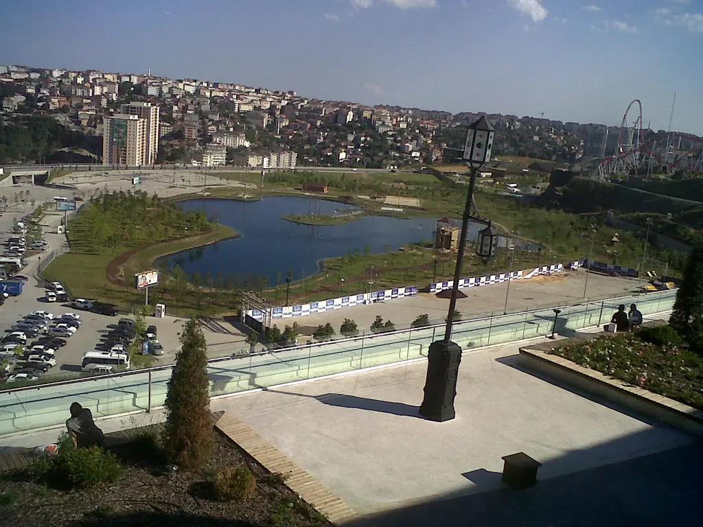 Vialand'in terasından aşağıdaki göl ve yeşil alan; çevresinde otopark, yollar, arkada tepelere yayılan mahalleler ve uzakta apartmanlar.