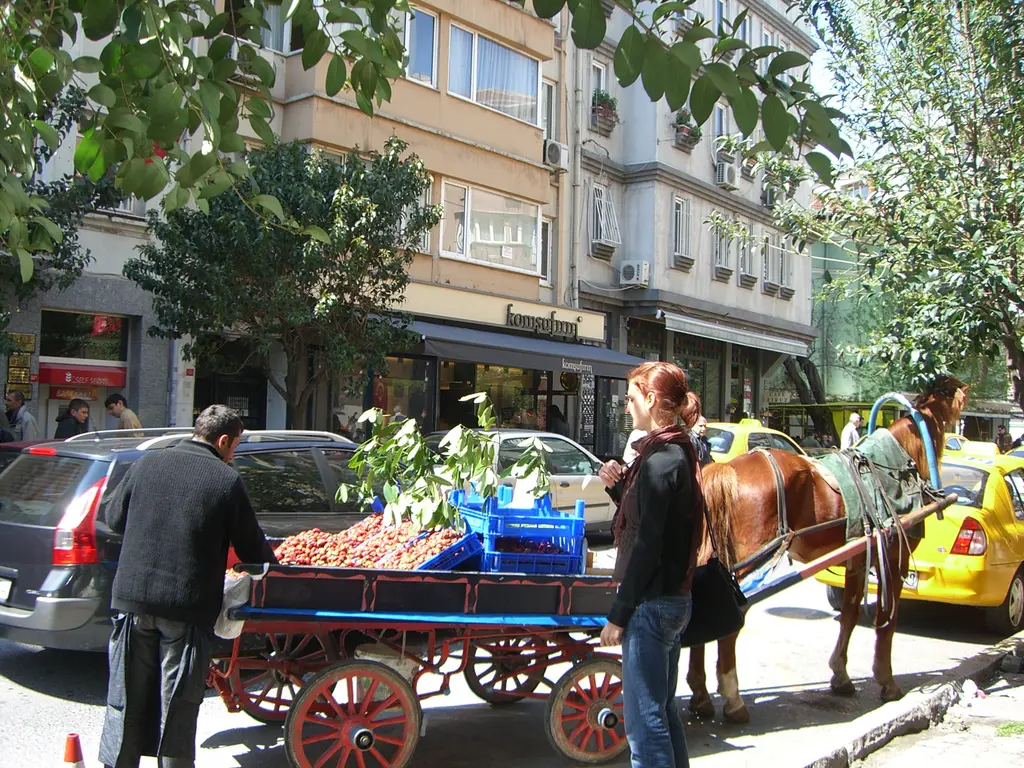 Cihangir'de at arabasıyla çilek satan seyyar satıcı; kasalarda çilekler, alıcılar, sarı taksi ve ağaçlı cadde.