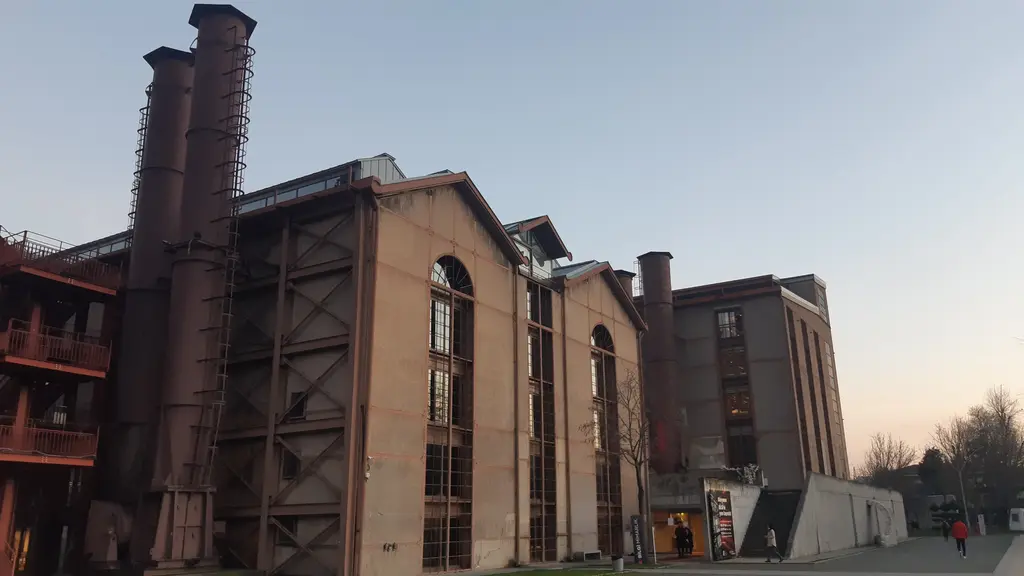 Santralistanbul'da makine dairesi; alacakaranlıkta tuğla cephe, kemerli pencereler, solda çelik iskeleli yüksek bacalar.