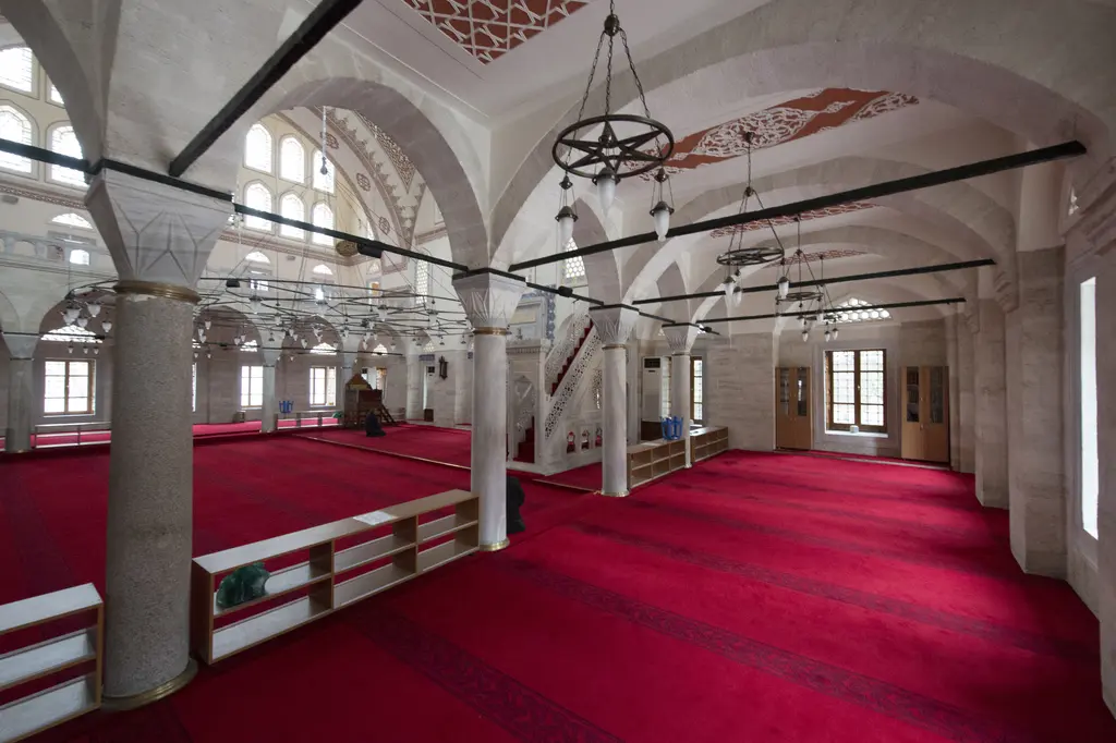 Zal Mahmud Paşa Camii'nde mahfil; kırmızı halı, ahşap korkuluklar, kalın sütunlar, düz tavandan sarkan avizeler ve pencereler.