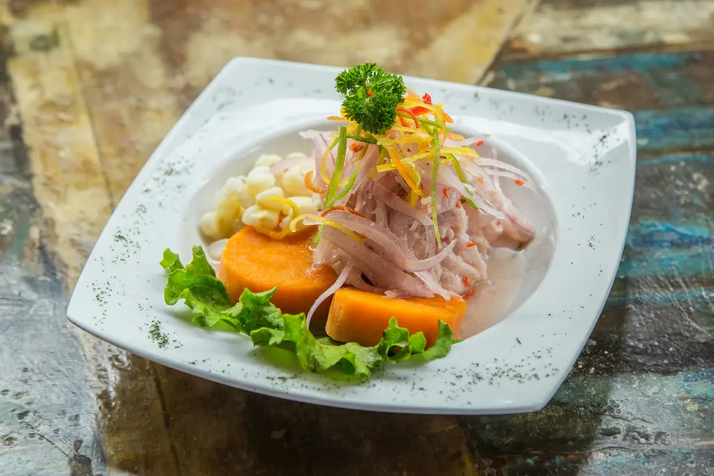 Peru mutfağından bir tabak ceviche; limonda terbiye edilmiş beyaz balık parçaları, yanında mısır taneleri ve tatlı patates dilimleri.