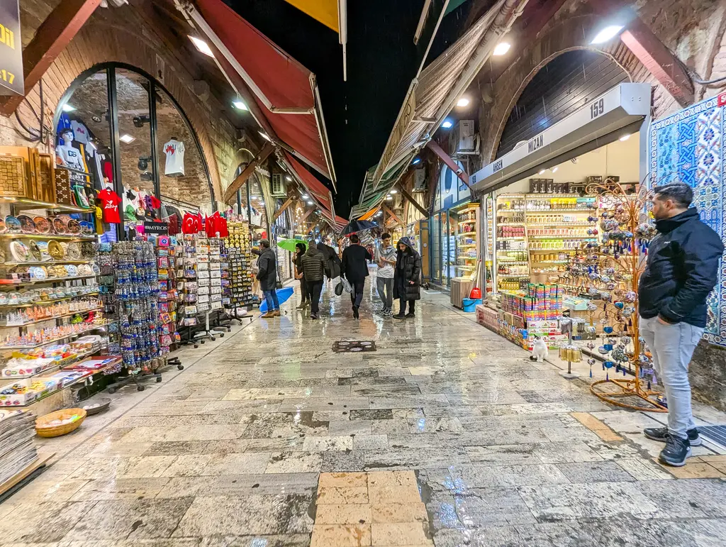Arasta Çarşısı'nda tuğla kemerli dükkânlar; vitrinlerde hediyelik eşya, tabaklar ve tekstil, önlerinde bekleyen esnaf ve yürüyen ziyaretçiler.