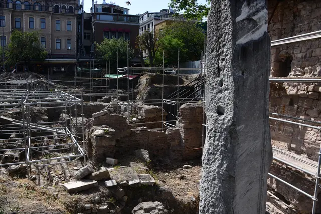 Sultanahmet'te Milyon Taşı; önde aşınmış mermer ayak, arkada iskeleler arasında Bizans duvar kalıntıları ve tuğla örgülü su terazisi.