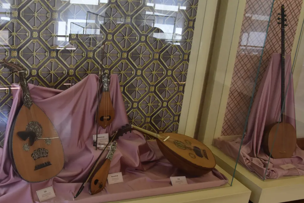Aynalıkavak Kasrı'nın alt katında çalgı vitrini; pembe kumaş üzerinde ud, uzun saplı çalgılar ve arkada süslemeli duvar.