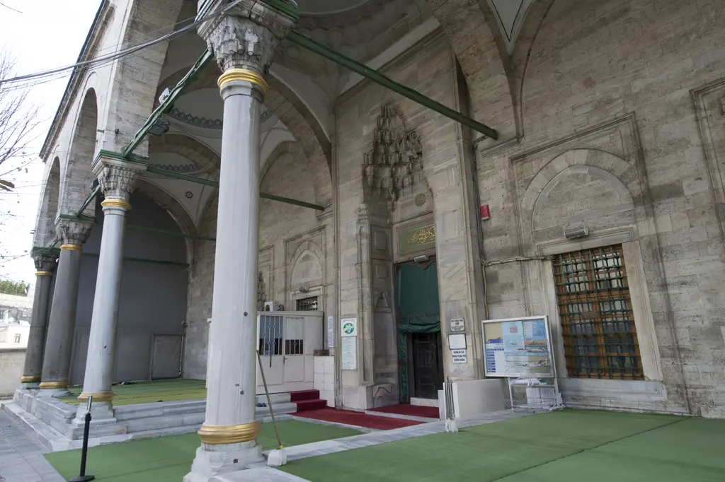 Gazi Atik Ali Paşa Camii'nin revak sütunları; yaldızlı bilezikli sütunlar, mukarnaslı başlıklar, arkada kapı nişi ve yeşil zemin.