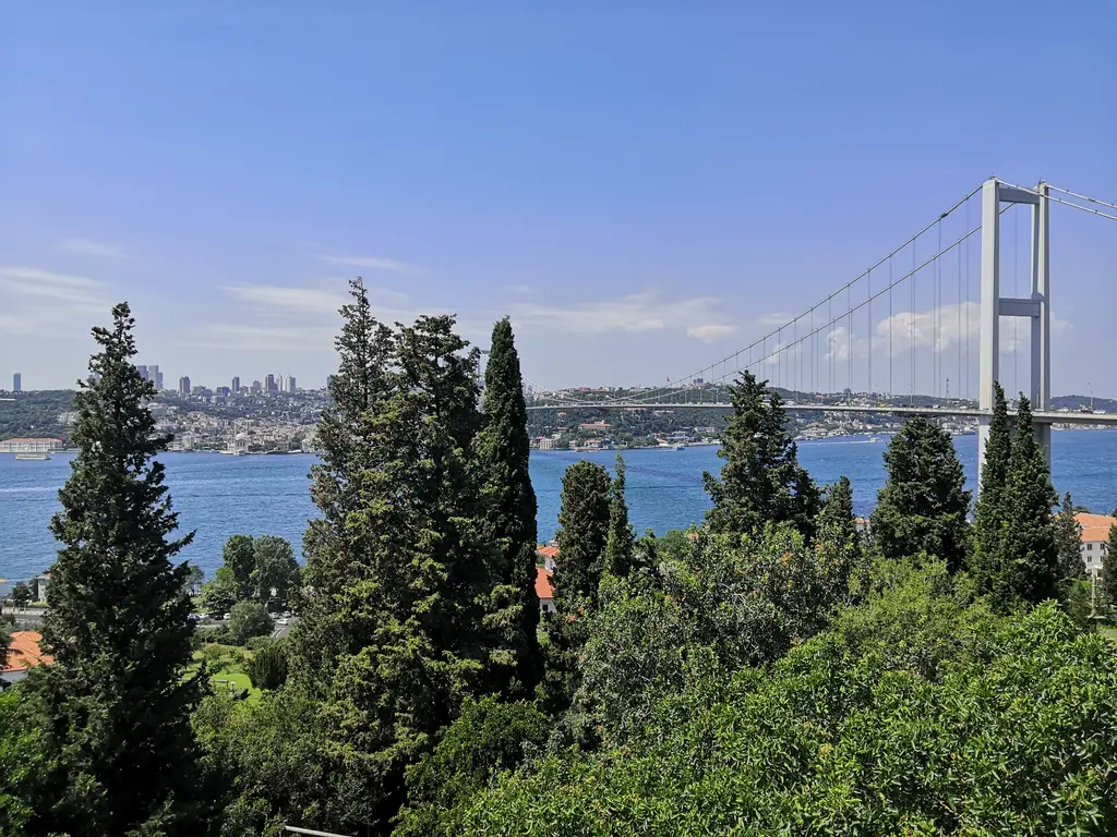 Mihrabat Tabiat Parkı'ndan Boğaz manzarası; önde sivri servi ağaçları, sağda Fatih Sultan Mehmet Köprüsü'nün kulesi, karşı kıyıda kentin silueti.