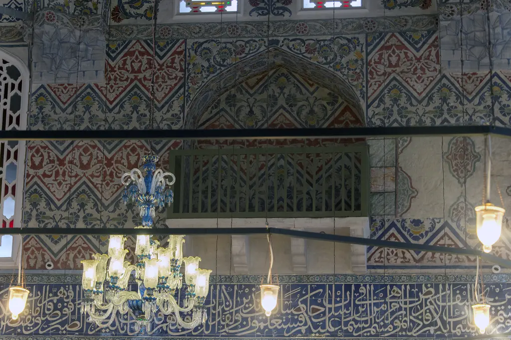 Sultan Ahmed Türbesi'nde kalem işi duvar; kırmızı ve lacivert zikzaklı desenler, kemerli niş içinde ahşap kafes, avize ve yazı kuşağı.