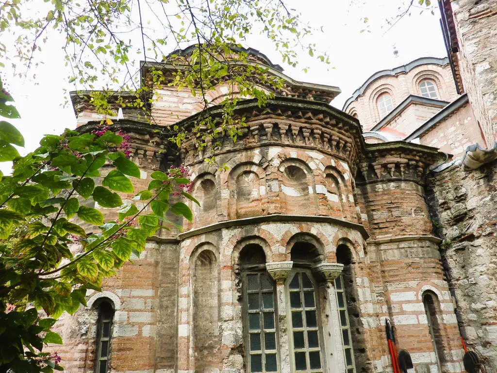 Fethiye Camii'nin doğu ucu ağaç dalları arasından; yan yana yuvarlak apsis çıkmaları, tuğla taş örgü ve üstte kubbe.