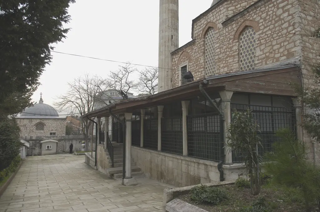Çinili Camii'nin son cemaat yeri; ahşap çatılı uzun revak, mermer sütunlar arasında demir şebekeler ve taş yol.