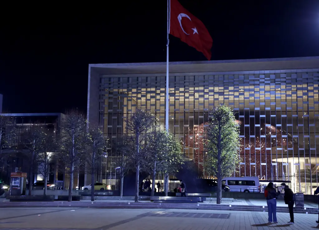 Gece Atatürk Kültür Merkezi; ışıklı ızgara desenli cephe, önünde aydınlatılmış ağaçlar, bayrak direği ve birkaç yaya.