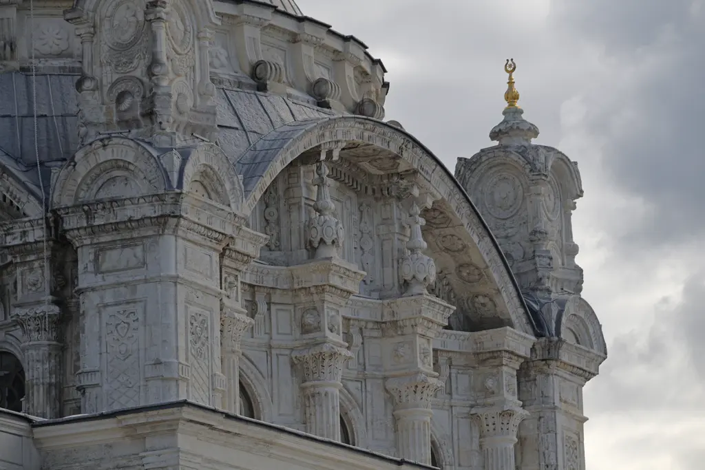 Ortaköy Camii'nin bir köşesi; oymalı taş cephe, kemer ve köşelerde süslü küçük kuleler, kapalı gökyüzü.