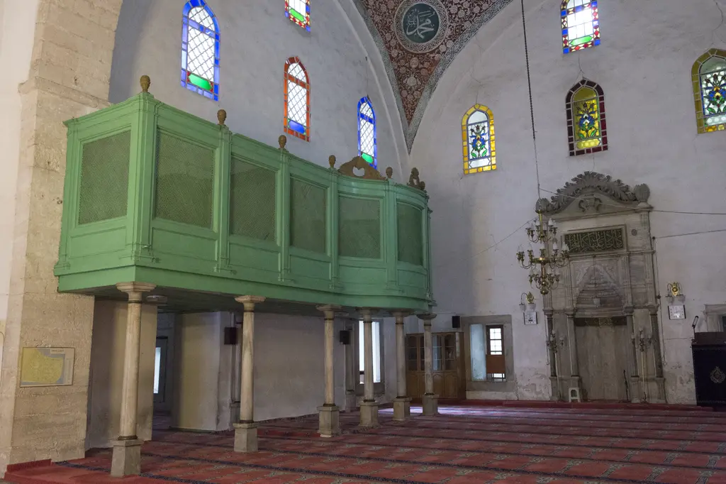 Mahmut Paşa Camii'nde yeşil boyalı hünkâr mahfili; ahşap kafesli loca, altında sütunlar, sağda mihrap, desenli halılar ve renkli camlar.