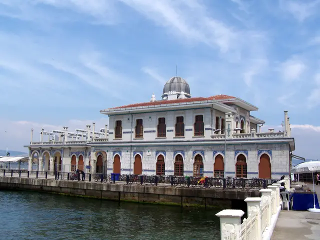 Adalar'da Büyükada iskelesi; kubbeli, sivri kemerli pencereli beyaz iskele binası, mavi deniz ve parçalı bulutlu gökyüzü.