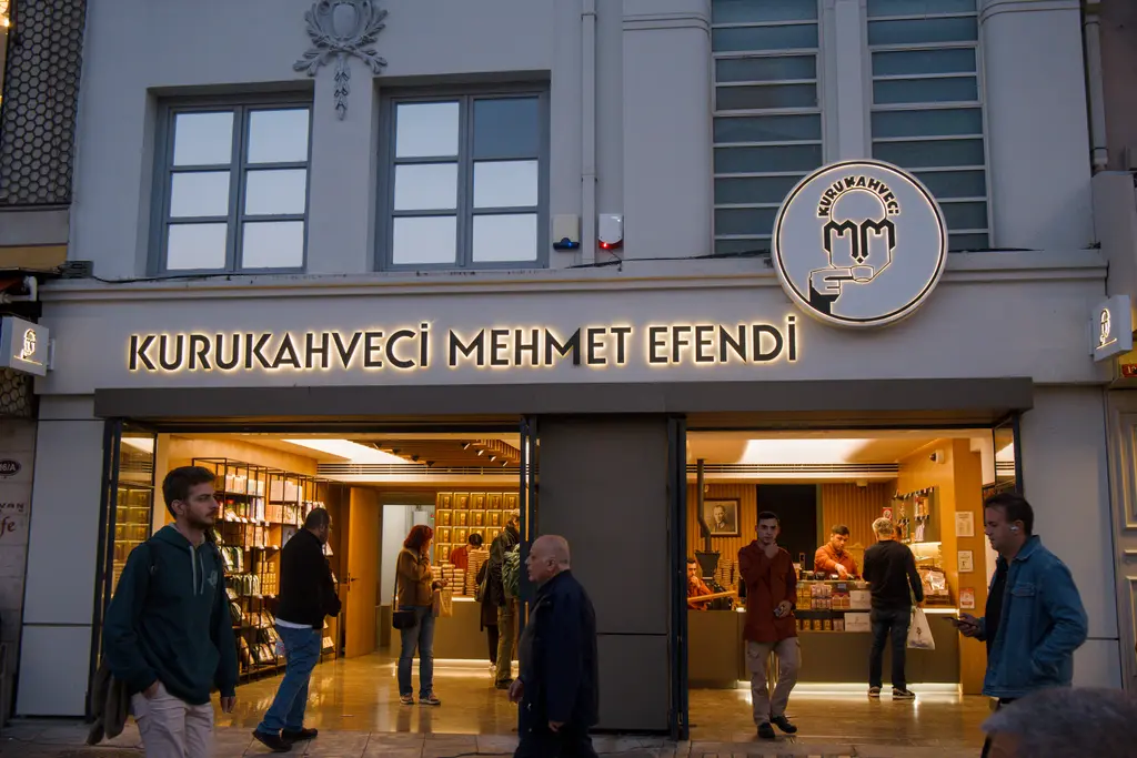 Kadıköy Çarşısı'nda Kurukahveci Mehmet Efendi; beyaz cephe, yuvarlak logo, aydınlık vitrin ve yürüyenler.