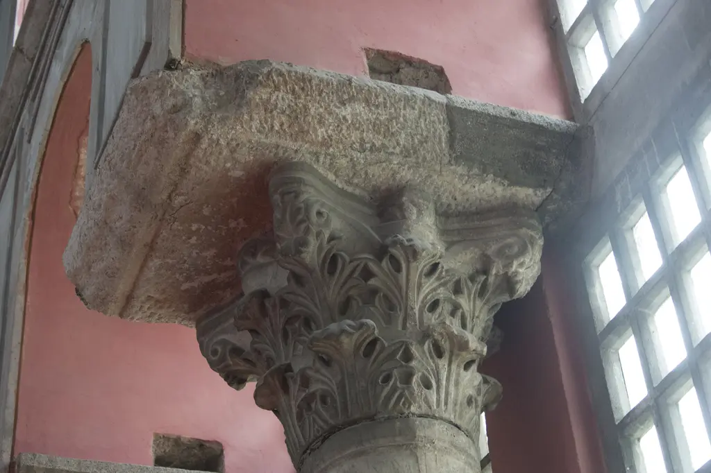 Kalenderhane Camii'nde mermer sütun başlığı; derin oyulmuş akantus yaprakları, üstünde kaba yontulu taş yastık ve arkada pembe sıvalı duvar.