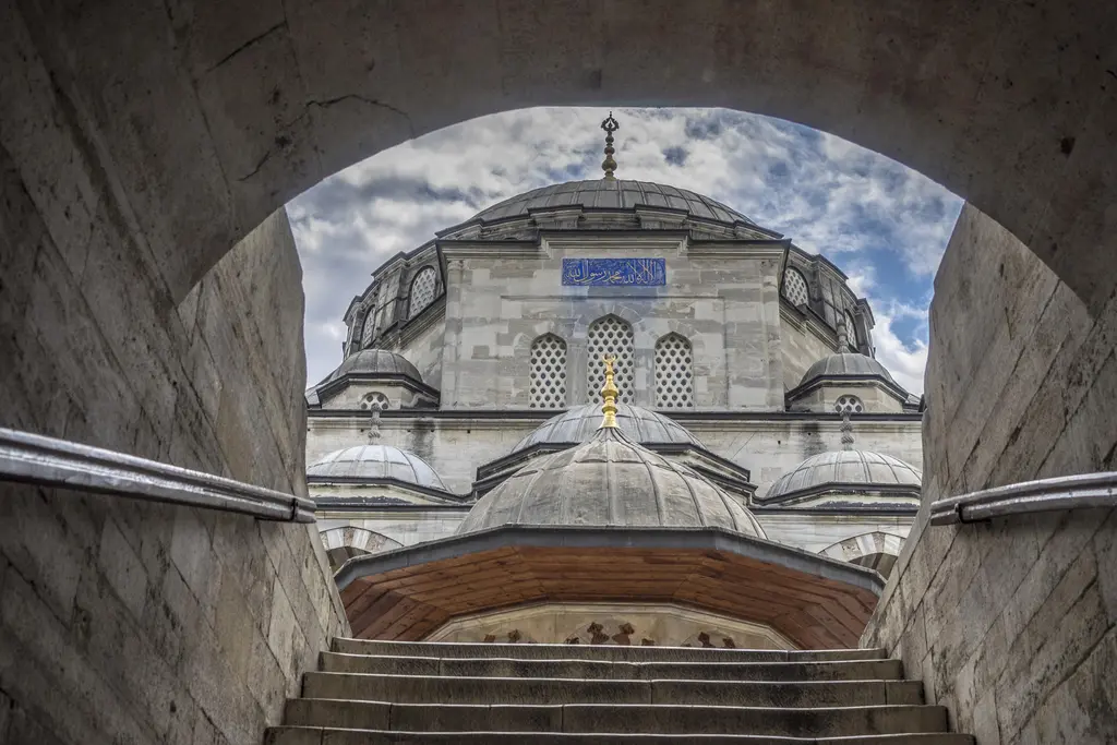 Sokullu Mehmed Paşa Camii'nde kapı altından avlu; kemerin çerçevelediği açıklıkta caminin kubbesi, basamaklar ve üstte açık gökyüzü.