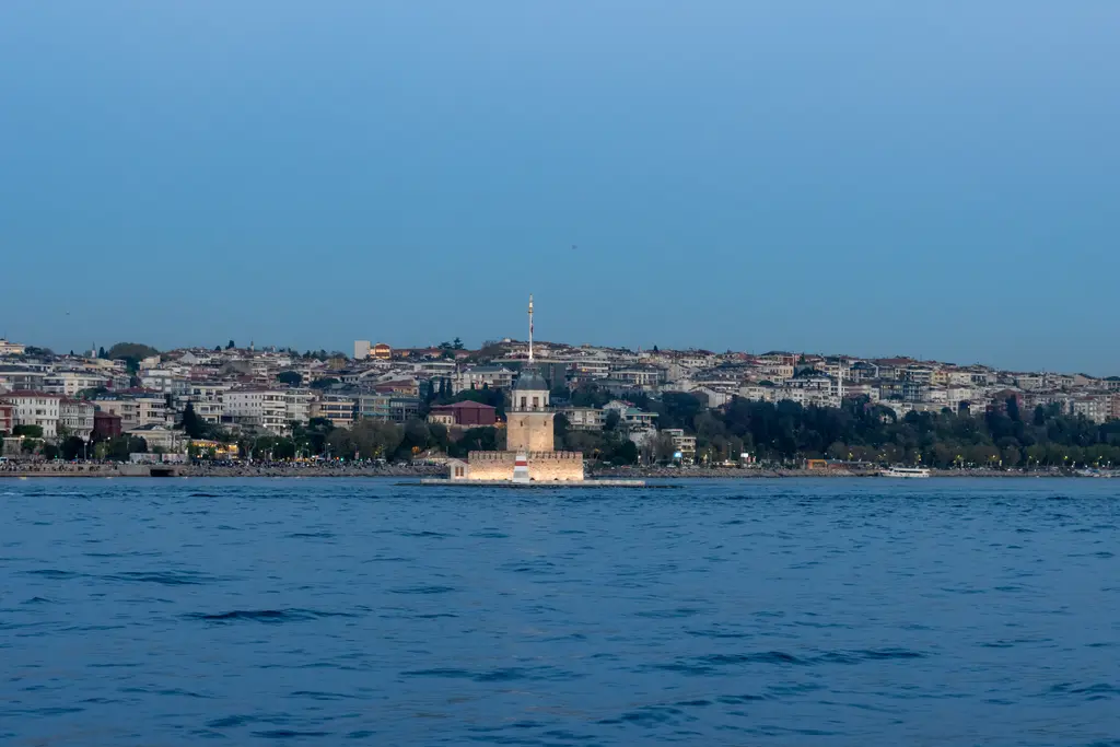 Denizden Üsküdar kıyısı; mavi su, kıyıda küçük Kız Kulesi ve yamaçlarda sıralanan evler.